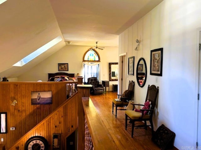 interior space with hardwood / wood-style floors, vaulted ceiling with skylight, ceiling fan, and wood walls