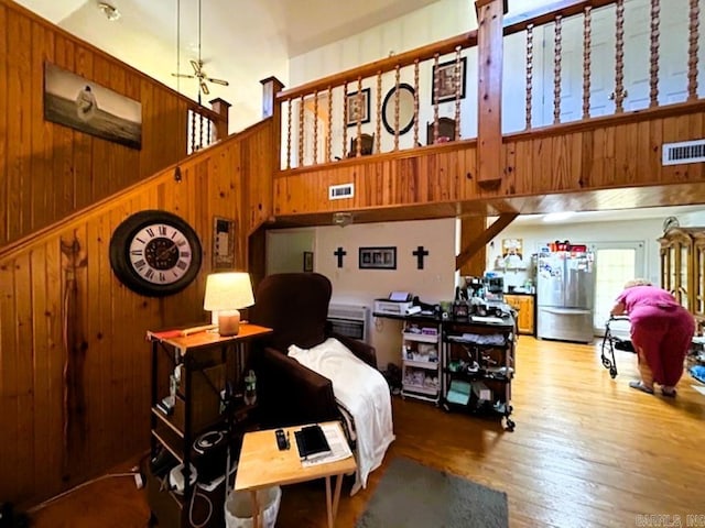 bedroom with high vaulted ceiling, wood walls, hardwood / wood-style floors, and stainless steel fridge