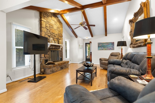 living room featuring a stone fireplace, beam ceiling, a healthy amount of sunlight, and light hardwood / wood-style floors