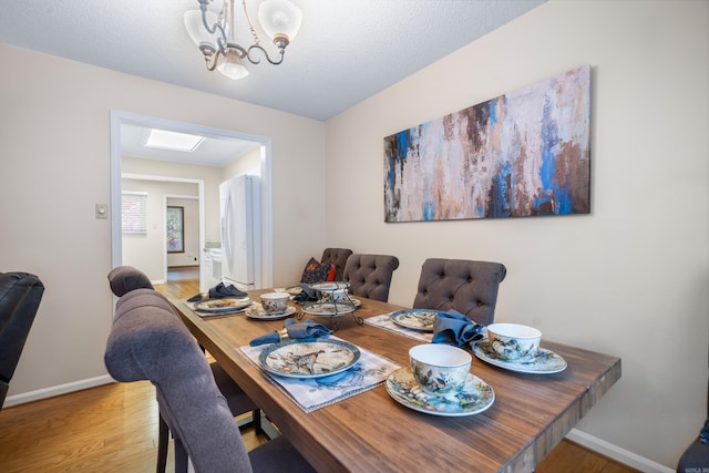 dining space featuring a chandelier, light hardwood / wood-style floors, and a skylight