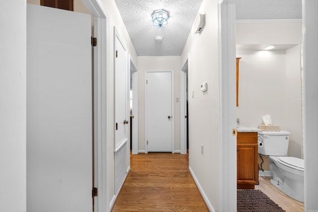 hallway with ornamental molding, a textured ceiling, and light wood-type flooring