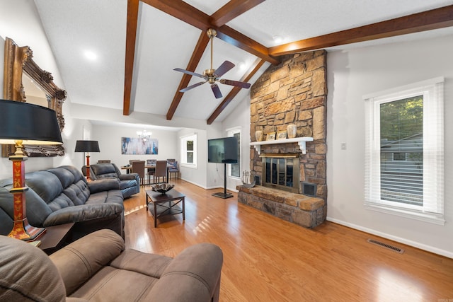 living room with a textured ceiling, hardwood / wood-style flooring, vaulted ceiling with beams, ceiling fan with notable chandelier, and a fireplace