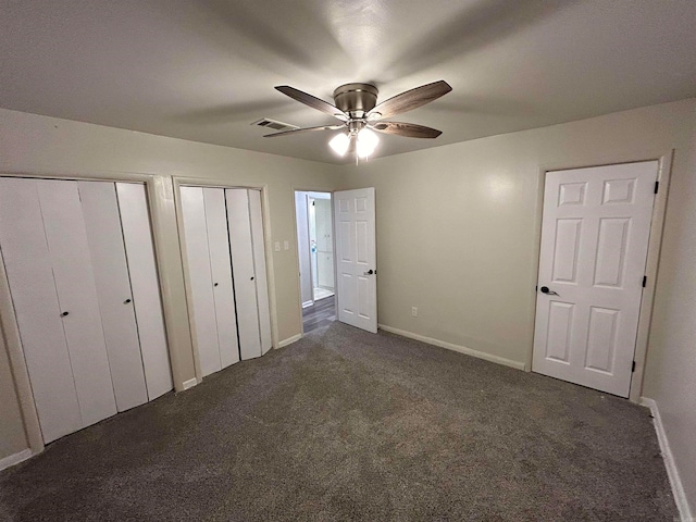 unfurnished bedroom with multiple closets, dark carpet, and ceiling fan