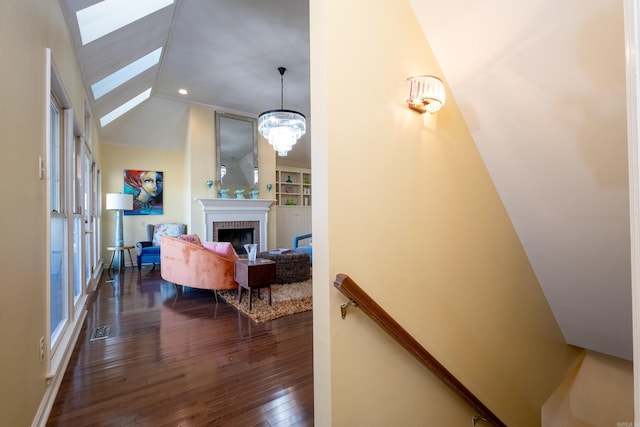 interior space featuring a notable chandelier, vaulted ceiling with skylight, dark hardwood / wood-style flooring, and a brick fireplace