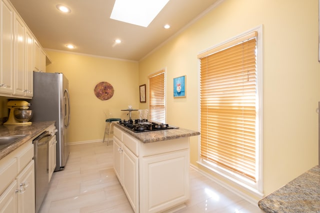 kitchen with white cabinets, appliances with stainless steel finishes, ornamental molding, a skylight, and a center island