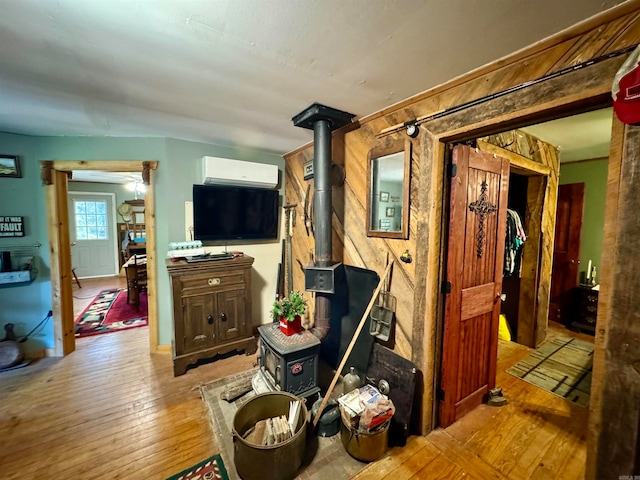 living room with a wood stove, a wall unit AC, light wood-type flooring, and wood walls