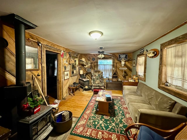 living room featuring a wood stove, hardwood / wood-style flooring, wooden walls, and ceiling fan