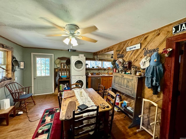 dining area with ceiling fan, hardwood / wood-style flooring, sink, wooden walls, and stacked washer / dryer