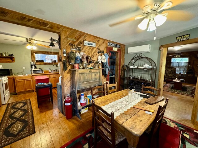 dining area featuring ceiling fan, wood walls, light hardwood / wood-style flooring, and a wall mounted air conditioner