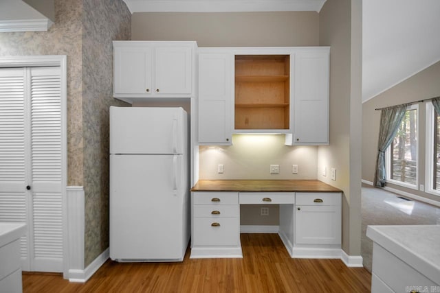 kitchen with built in desk, white cabinets, white fridge, ornamental molding, and light hardwood / wood-style flooring