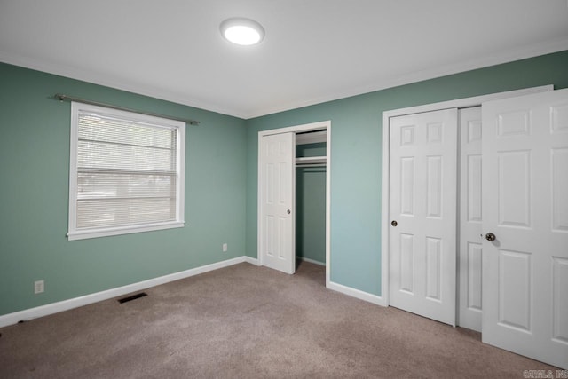 unfurnished bedroom featuring crown molding, two closets, and light colored carpet