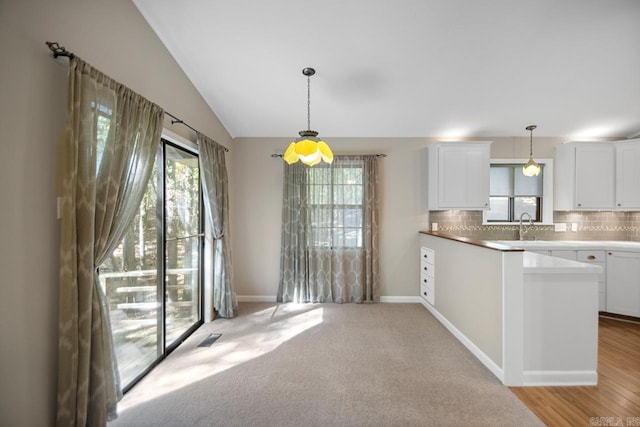 kitchen featuring lofted ceiling, light hardwood / wood-style flooring, pendant lighting, white cabinetry, and tasteful backsplash