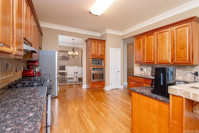 kitchen featuring ornamental molding, an inviting chandelier, appliances with stainless steel finishes, light hardwood / wood-style floors, and tasteful backsplash