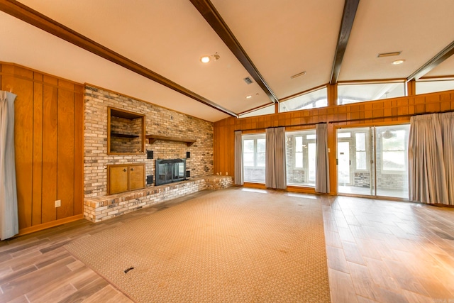 unfurnished living room featuring wooden walls, light hardwood / wood-style flooring, vaulted ceiling with beams, and a fireplace