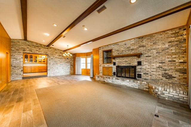 unfurnished living room featuring hardwood / wood-style flooring, brick wall, lofted ceiling with beams, a notable chandelier, and a fireplace