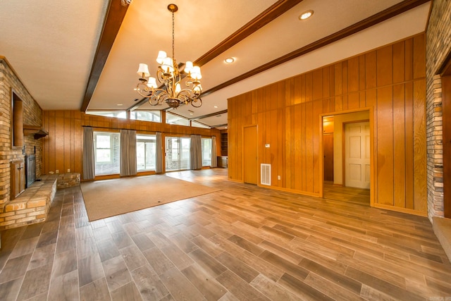 unfurnished living room featuring an inviting chandelier, wood-type flooring, vaulted ceiling with beams, a fireplace, and wooden walls