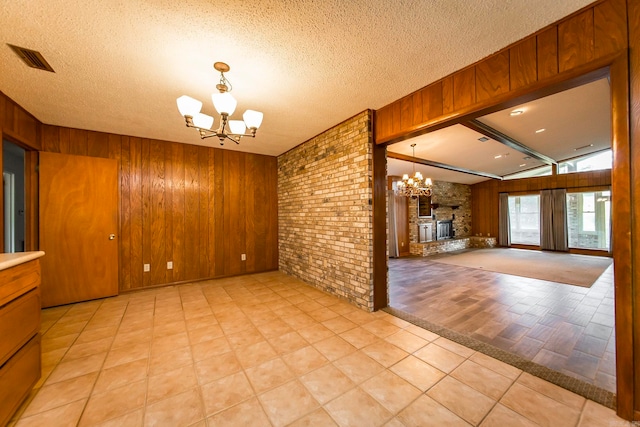 spare room featuring lofted ceiling with beams, a textured ceiling, an inviting chandelier, and a fireplace