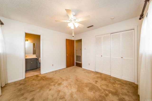 unfurnished bedroom featuring a closet, light carpet, a textured ceiling, ensuite bathroom, and ceiling fan