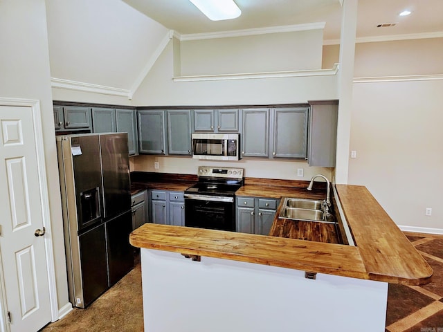 kitchen with a peninsula, butcher block countertops, a sink, ornamental molding, and appliances with stainless steel finishes