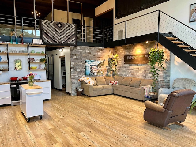 living room with brick wall, a towering ceiling, and light hardwood / wood-style flooring