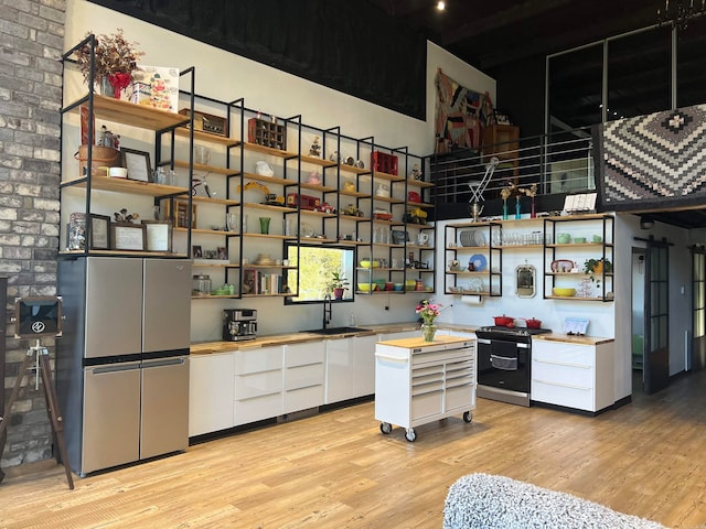 kitchen featuring white cabinets, appliances with stainless steel finishes, light wood-type flooring, sink, and brick wall