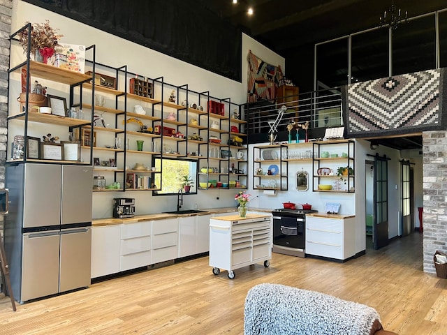 kitchen with a towering ceiling, appliances with stainless steel finishes, sink, light wood-type flooring, and white cabinetry