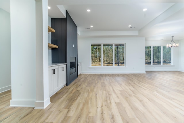 unfurnished living room with light wood-style floors, recessed lighting, baseboards, and an inviting chandelier