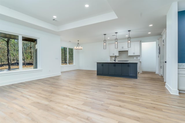 kitchen featuring a center island with sink, white cabinets, open floor plan, hanging light fixtures, and light countertops