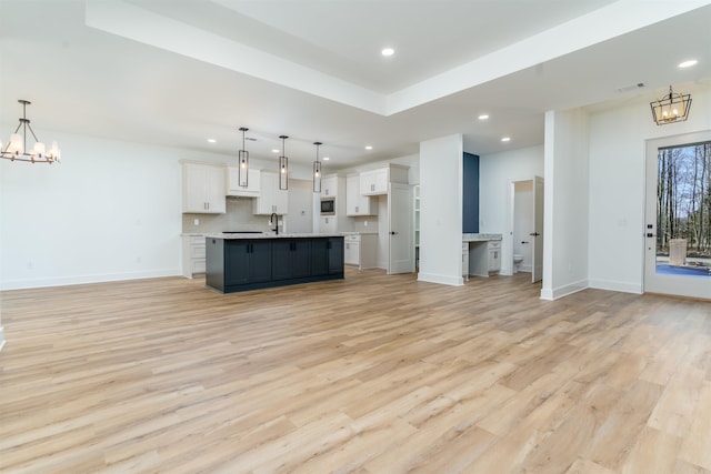 unfurnished living room with baseboards, light wood-type flooring, a sink, and a notable chandelier