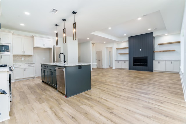 kitchen with appliances with stainless steel finishes, open floor plan, white cabinets, and hanging light fixtures