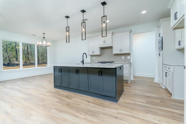 kitchen with white cabinetry, hanging light fixtures, tasteful backsplash, stainless steel microwave, and an island with sink