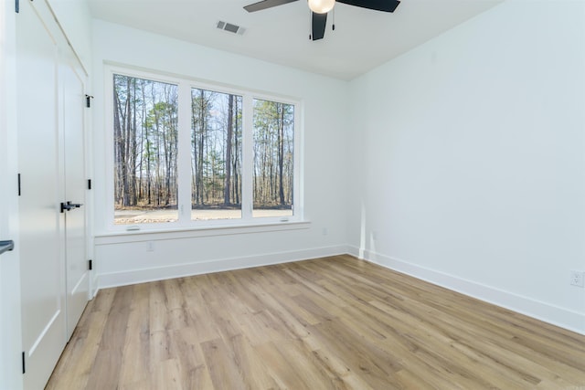 empty room with visible vents, ceiling fan, light wood finished floors, and baseboards