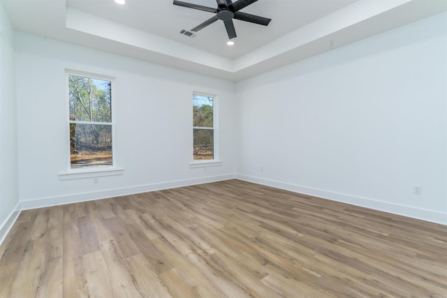 empty room featuring light wood finished floors, baseboards, and a tray ceiling