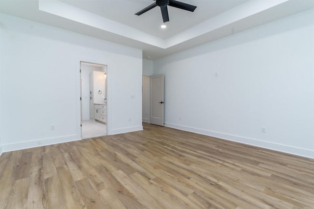 unfurnished bedroom featuring ensuite bathroom, recessed lighting, baseboards, light wood-style floors, and a raised ceiling