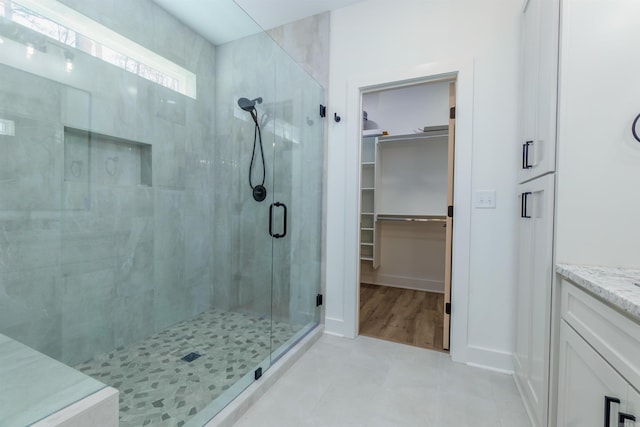 full bathroom featuring a spacious closet, a shower stall, vanity, and baseboards