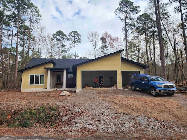 view of front of property featuring a garage, a shingled roof, and dirt driveway