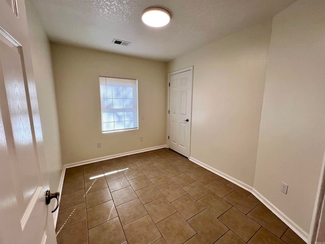 tiled empty room featuring a textured ceiling