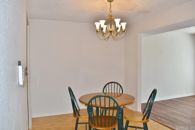 dining room with light hardwood / wood-style flooring, a textured ceiling, and a notable chandelier