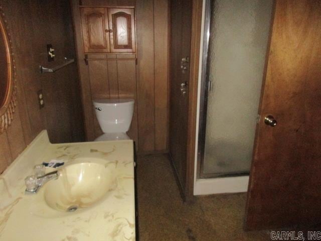 bathroom featuring toilet, walk in shower, wooden walls, and vanity