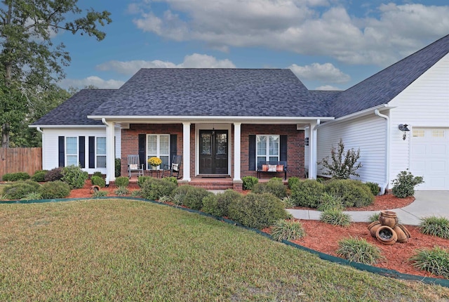 view of front of home with a shingled roof, covered porch, an attached garage, a front lawn, and brick siding