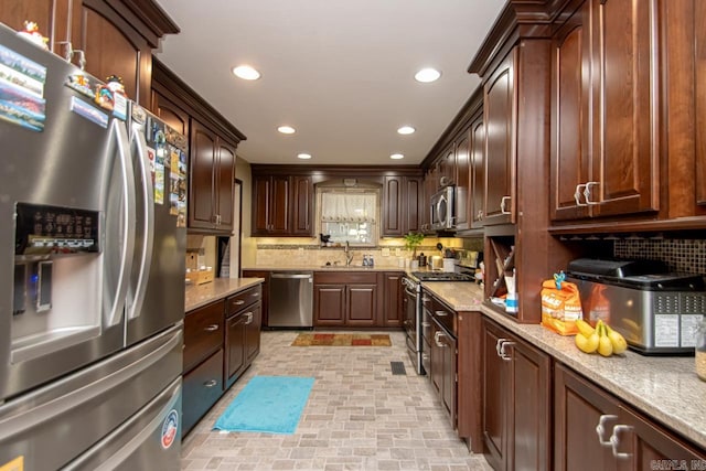 kitchen featuring decorative backsplash, dark brown cabinets, light stone counters, sink, and stainless steel appliances