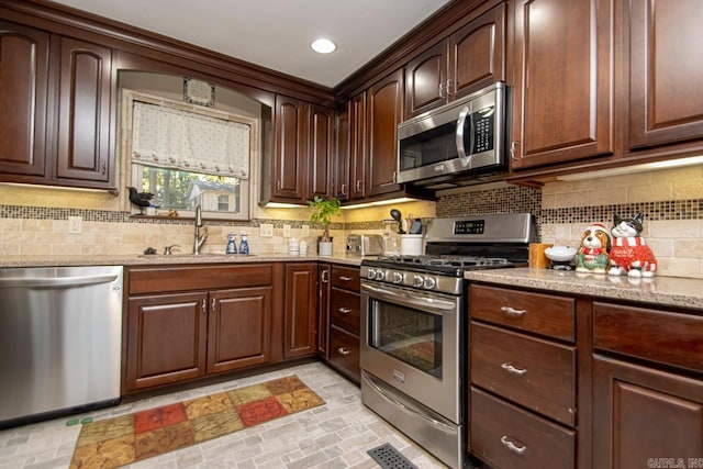 kitchen featuring decorative backsplash, dark brown cabinets, light stone counters, appliances with stainless steel finishes, and sink