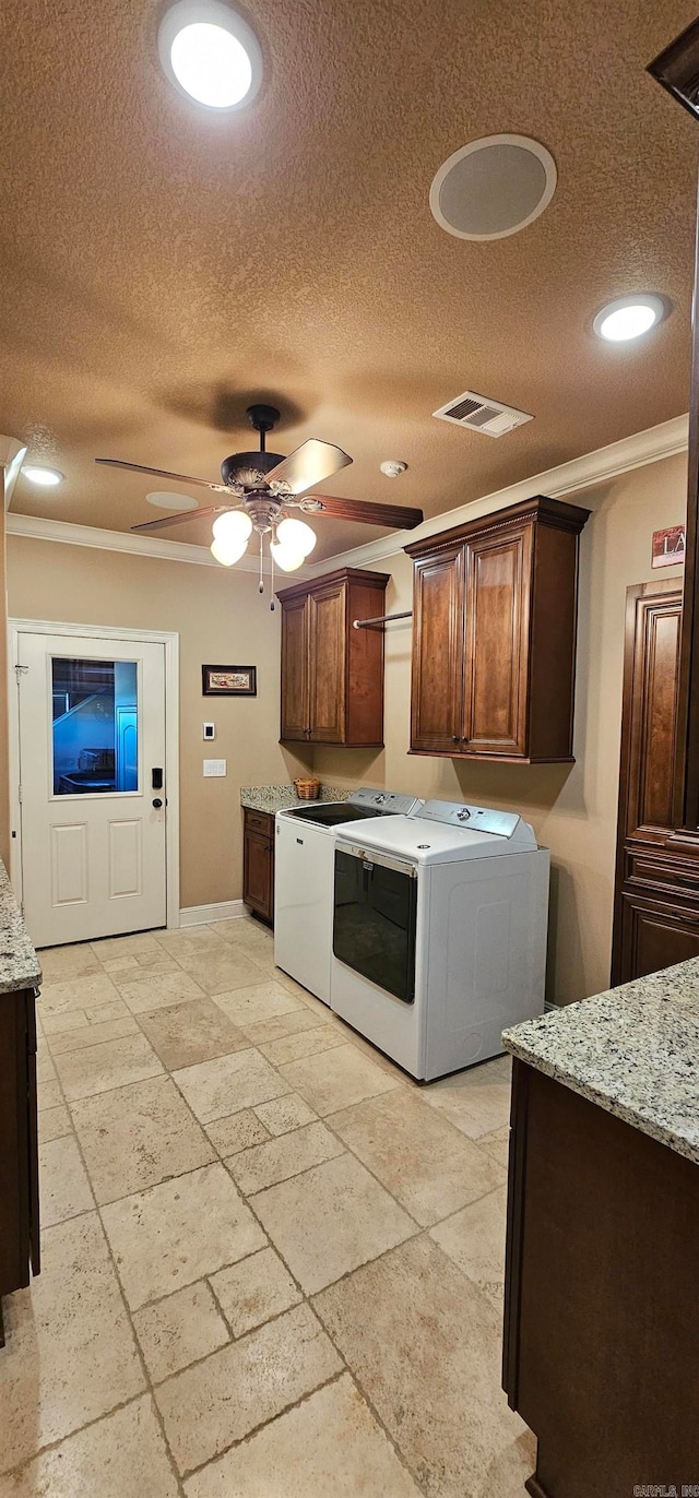 kitchen with ornamental molding, a textured ceiling, light stone counters, and washer and clothes dryer