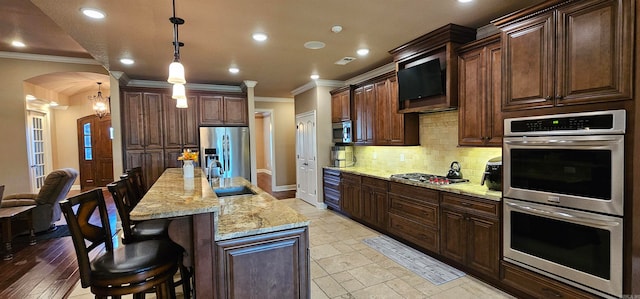 kitchen with sink, hanging light fixtures, a kitchen breakfast bar, stainless steel appliances, and ornamental molding