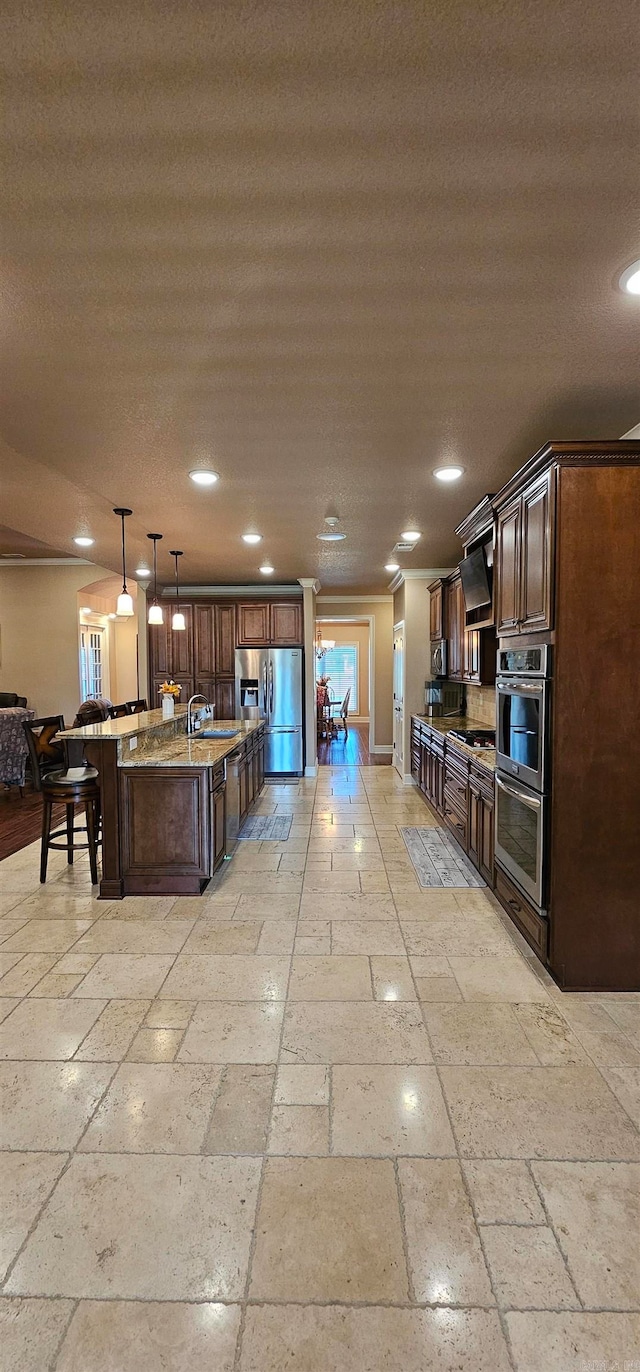 kitchen featuring a large island with sink, sink, a kitchen bar, hanging light fixtures, and stainless steel appliances