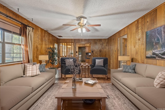 living room with wood walls, hardwood / wood-style floors, a textured ceiling, and ceiling fan