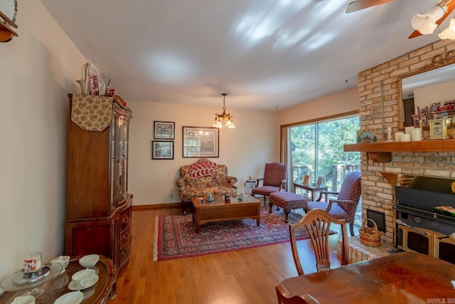 living room with a textured ceiling, a brick fireplace, hardwood / wood-style flooring, and a chandelier