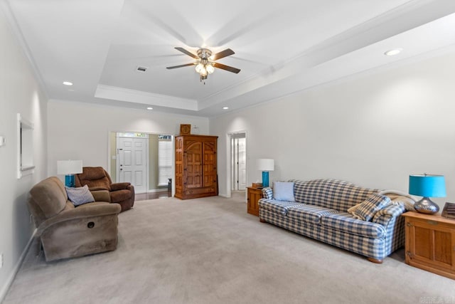 living room with ceiling fan, crown molding, a tray ceiling, and light colored carpet