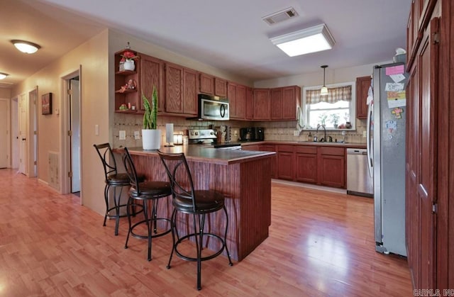 kitchen with kitchen peninsula, appliances with stainless steel finishes, light hardwood / wood-style flooring, and pendant lighting