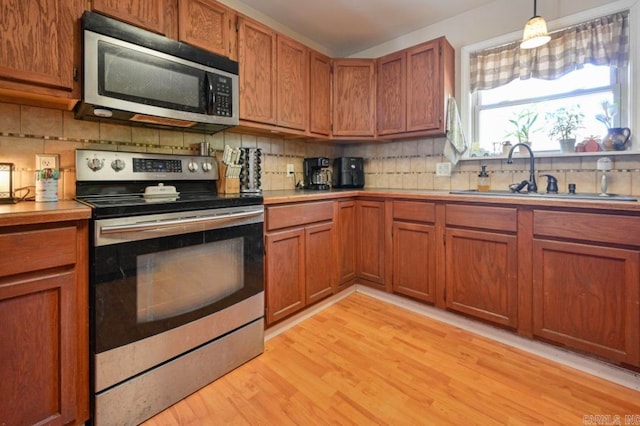 kitchen featuring tasteful backsplash, appliances with stainless steel finishes, light wood-type flooring, sink, and decorative light fixtures